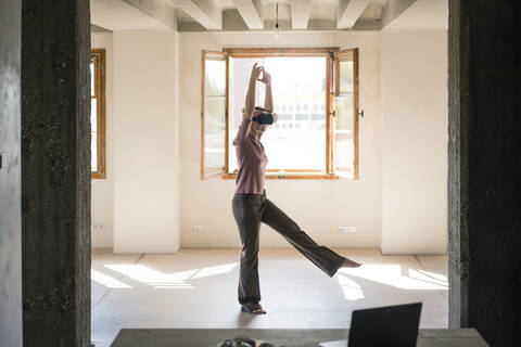 Frau tanzt, während sie zu Hause ein Video im Virtual-Reality-Simulator betrachtet, lizenzfreies Stockfoto