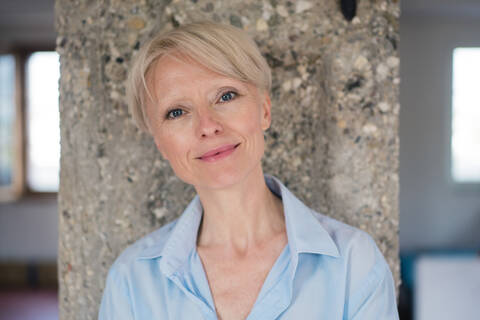 Smiling businesswoman with blue eyes against column at home stock photo