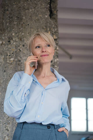 Lächelnde Geschäftsfrau, die mit einem Mobiltelefon spricht, während sie an einer Säule steht, lizenzfreies Stockfoto