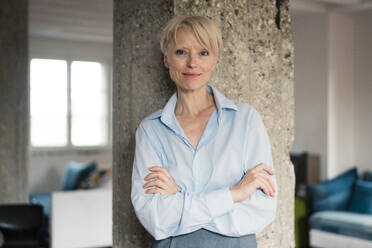 Smiling businesswoman with arms crossed leaning on column at home - MOEF03590