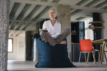 Smiling businesswoman with crossed legs holding digital tablet while sitting at home - MOEF03606