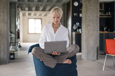 Unternehmerin, die einen Laptop benutzt, während sie zu Hause auf einem Sitzsack sitzt - MOEF03609