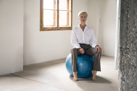 Frau meditiert auf einem Fitnessball sitzend zu Hause, lizenzfreies Stockfoto