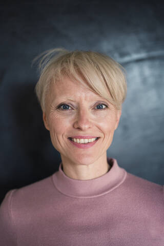 Lächelnde blonde Frau mit blauen Augen an der Wand, lizenzfreies Stockfoto