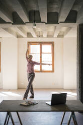 Woman dancing against window in loft apartment - MOEF03639