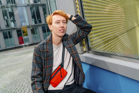 Redhead man with hand in hair on footpath against building stock photo