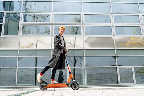 Man riding electric push scooter on footpath by building - OGF00901