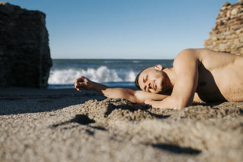 Mann ohne Hemd liegt entspannt am Strand - MIMFF00570