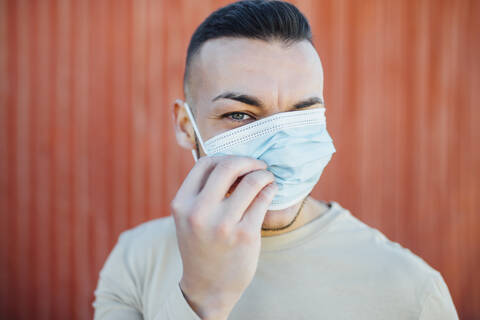 Mid adult man covering his face with protective face mask while standing against red wall stock photo