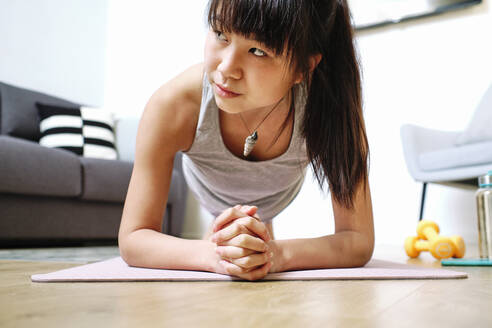 Woman practicing plank position on exercise mat at home - AODF00319