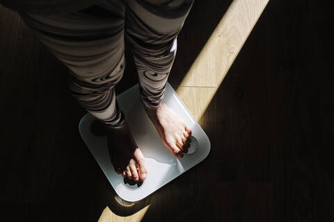 Young woman standing on weight scale in dark at home stock photo