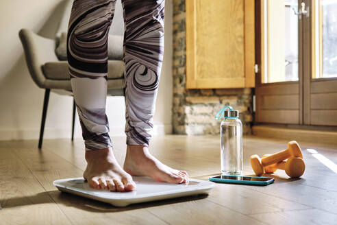 Woman analyzing weight while standing on weight scale at home - AODF00327