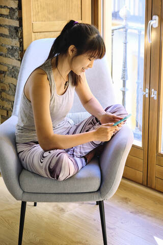 Woman using mobile phone while sitting on chair at home stock photo