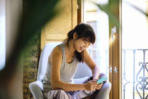 Smiling woman using mobile phone while sitting on chair at home stock photo