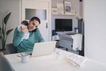 Mann mit kleinem Jungen, der mit dem Handy telefoniert, während er einen Laptop am Schreibtisch im Heimbüro benutzt - MPPF01528