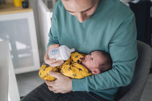 Father feeding milk through bottle while sitting at home - MPPF01536