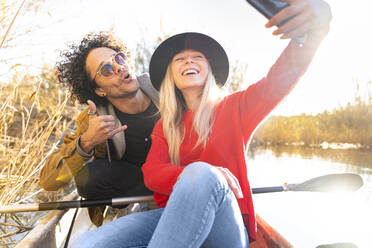 Junges Paar, das ein Selfie mit dem Mobiltelefon macht, während es im Kanu sitzt - SBOF02676