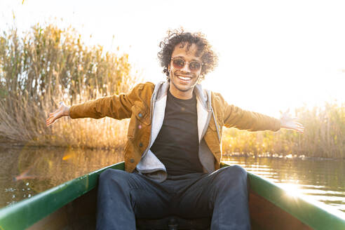 Lächelnder Mann sitzt mit ausgestreckten Armen in einem Kanu auf einem Fluss - SBOF02681