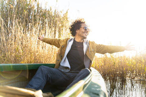 Carefree man with arms outstretched smiling while sitting in canoe on river stock photo