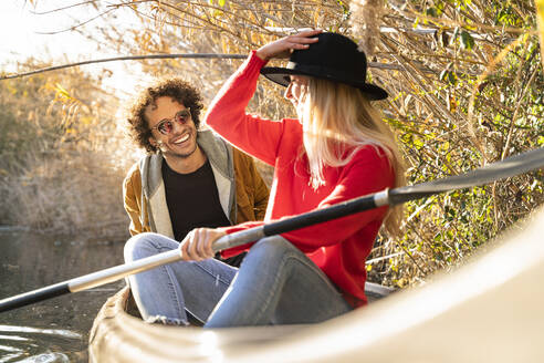 Woman adjusting hat while sitting with man in canoe on river - SBOF02688