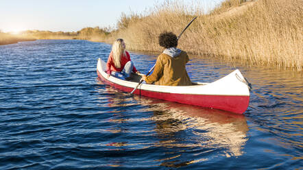Boyfriend canoeing with girlfriend on river during sunset - SBOF02703