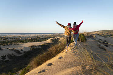Paar mit Arm um läuft zusammen auf Sanddüne während Sonnenuntergang - SBOF02707