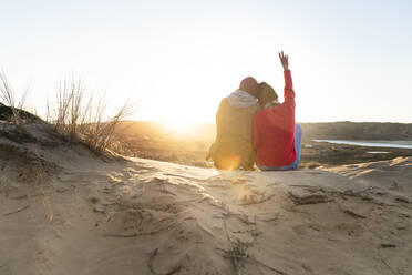 Frau mit erhobener Hand, die das Friedenszeichen zeigt, während sie mit einem Mann auf einer Sanddüne sitzt - SBOF02710