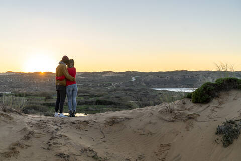 Young couple looking at sunset view while standing on sand dune stock photo