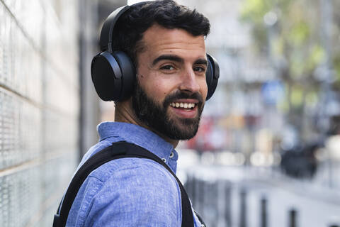 Lächelnder junger Geschäftsmann hört Musik über drahtlose Kopfhörer, lizenzfreies Stockfoto