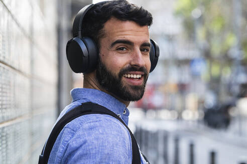 Smiling young businessman listening music through wireless headphones - PNAF00752
