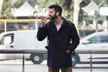 Young male entrepreneur talking on mobile phone through speaker against vehicle - PNAF00761