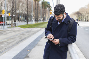 Männlicher Geschäftsmann, der ein digitales Tablet benutzt und sich am Geländer eines Bahnhofs anlehnt - PNAF00762