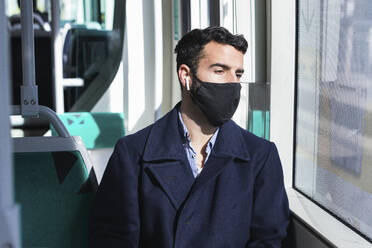 Male commuter sitting in train while looking through window during COVID-19 - PNAF00769