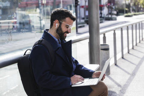 Male freelancer working on laptop while sitting on bench at station stock photo