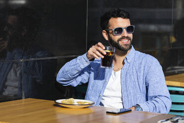 Lächelnder junger Geschäftsmann, der einen schwarzen Kaffee trinkt, während er in einem Straßencafé sitzt - PNAF00776