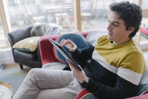 Mann benutzt ein digitales Tablet, während er auf dem Sofa im Wohnzimmer sitzt - BOYF01929