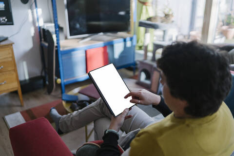 Mittlerer Mann, der ein digitales Tablet benutzt, während er zu Hause auf dem Sofa sitzt, lizenzfreies Stockfoto