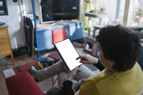 Mittlerer Mann, der ein digitales Tablet benutzt, während er zu Hause auf dem Sofa sitzt - BOYF01930
