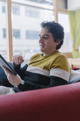 Mann sitzt auf dem Sofa und benutzt ein digitales Tablet im Wohnzimmer - BOYF01931