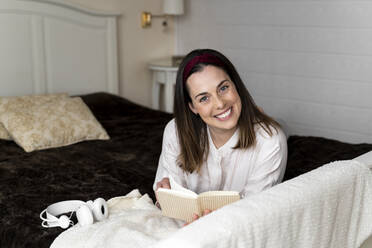 Lächelnde Frau mit Buch auf dem Bett liegend zu Hause - AFVF08224
