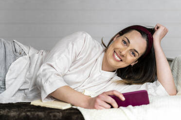 Beautiful smiling woman with smart phone lying on bed - AFVF08225