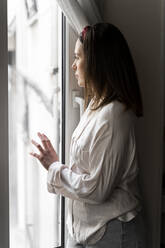 Thoughtful young woman looking though window while standing at home - AFVF08229