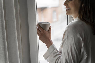 Lächelnde Frau mit Kaffee am Fenster stehend - AFVF08232