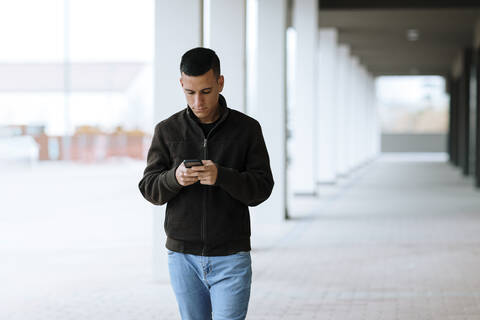 Young man using smart phone while walking on footpath stock photo