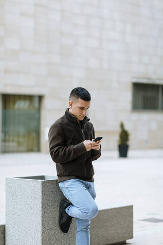 Young man using smart phone while standing against building stock photo