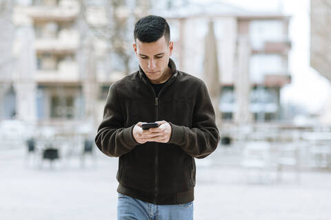 Young man using mobile while walking against building stock photo