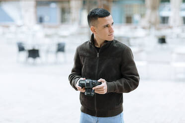 Junger männlicher Fotograf mit Kamera, der wegschaut - OCAF00637