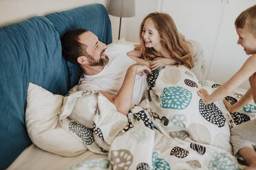 Smiling daughter and son having fun with father on bed at home - GMLF00996