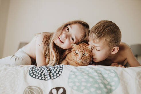 Smiling girl with brother leaning on cat in bedroom at home - GMLF01000