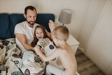 Playful children with father on bed at home - GMLF01001